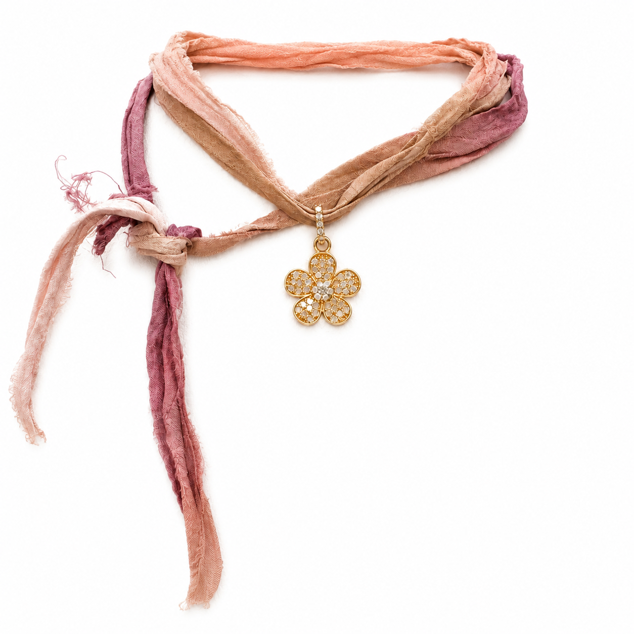 A delicate multi-strand scarf necklace in soft peach, tan, and dusty rose tones, featuring a gold-tone flower-shaped pendant with clear crystals, set against a plain white background.